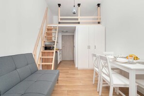 Ein kompakter Wohnraum mit Sofa, Esstisch, Stühlen, einer Treppe und einer Küchenzeile.