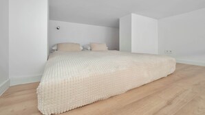 Un dormitorio con cama, paredes blancas y suelo de madera.