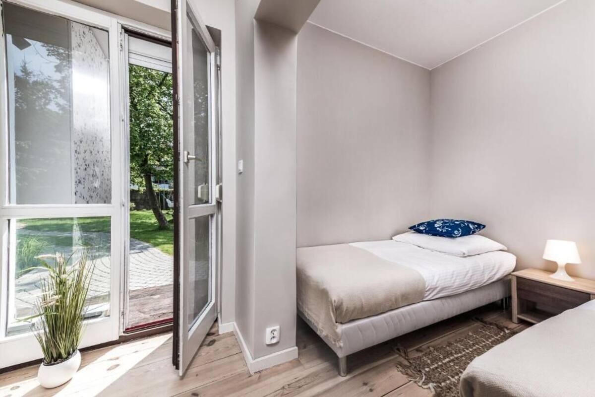 A bedroom with a bed, bedside table, lamp, and a sliding glass door leading to a garden.