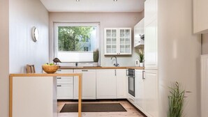 A modern kitchen with white cabinets, a wooden table, a window with a view, and a potted plant.