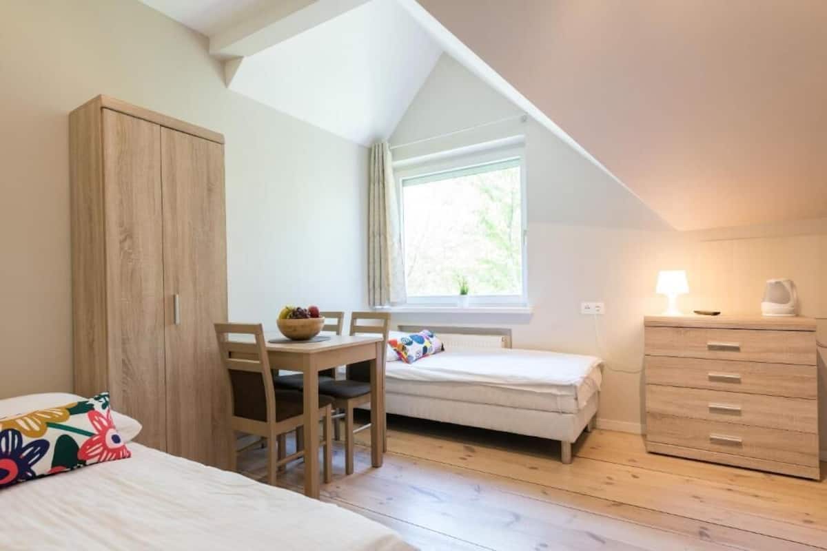 A bedroom with a loft bed, a desk with a chair, a bedside table, and a dresser.
