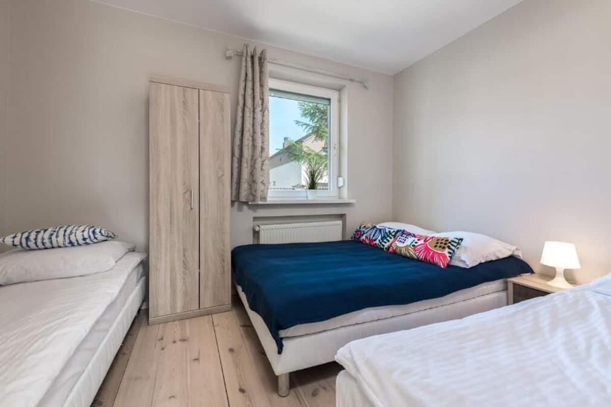 A bedroom with two beds, a window with curtains, a bedside lamp, and a radiator.