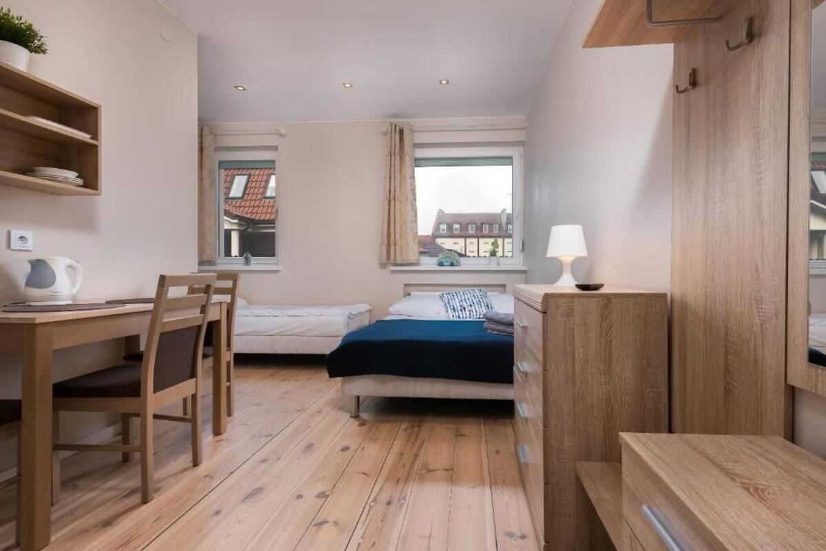 A compact room with a bed, a desk, a chair, a lamp, and a window with a view of buildings.
