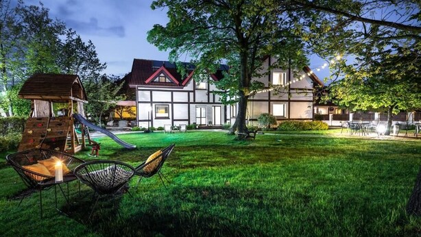 A house with a climbing wall, a slide, and a grassy yard with outdoor furniture.