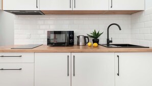 A modern kitchen with white cabinets, a microwave, a kettle, and a sink. - Functional Studio with Mezzanine | Łódź Center (Łódź)