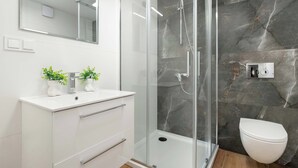A modern bathroom with a glass-enclosed shower, white vanity, and marble walls. - Functional Studio with Mezzanine | Łódź Center (Łódź)