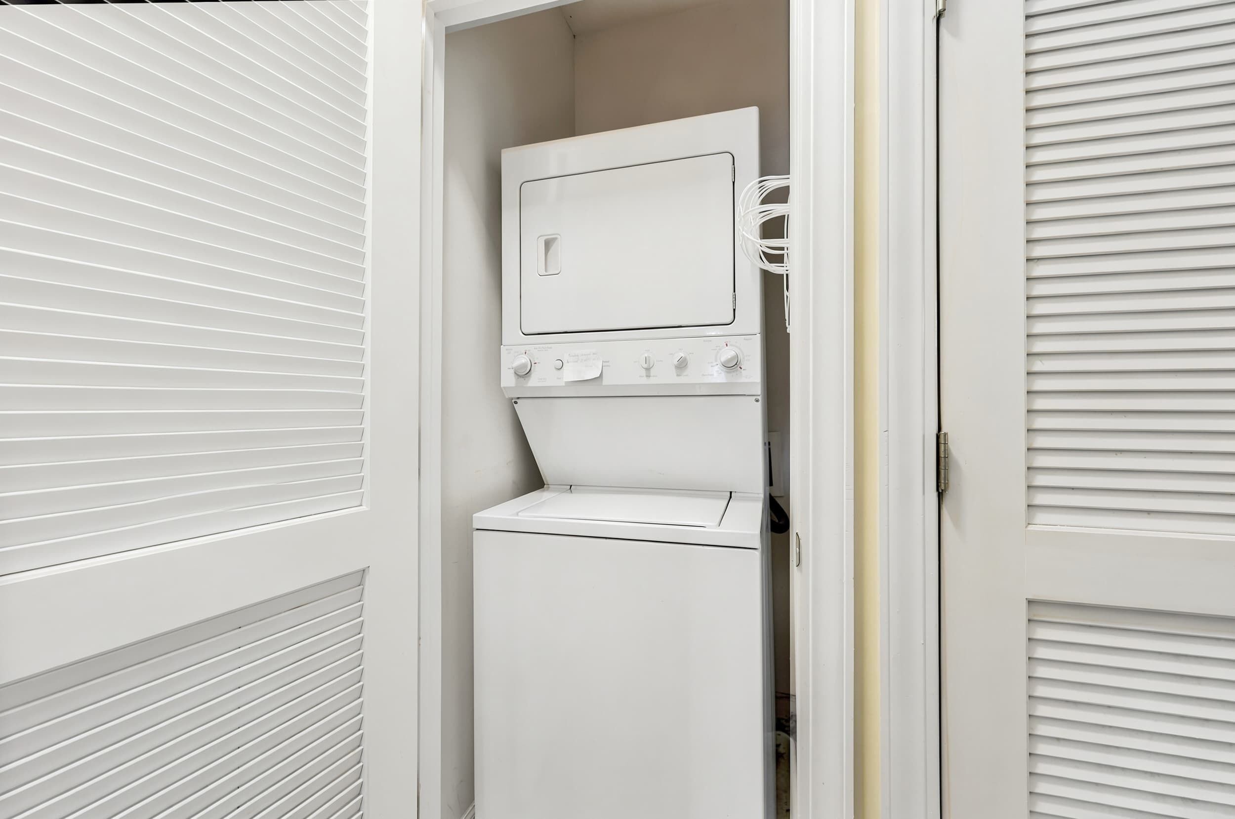 A compact laundry room with a washer and dryer, a control panel, and a power cord.