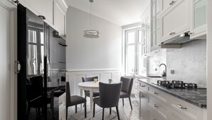 A modern kitchen with white cabinetry, a round dining table with chairs, and a patterned floor. - Grand Belle Sopot - Near the beach (Sopot)