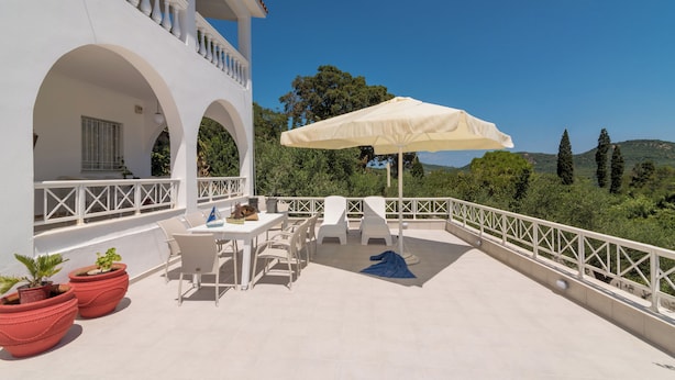 A white building with a balcony, outdoor seating, and a view of the landscape. - Amalia Country House (Zakynthos)