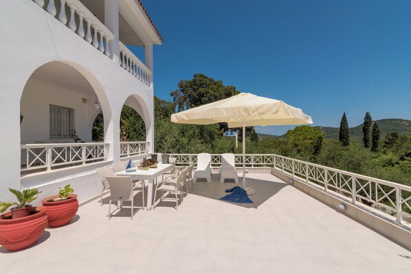 A white building with a balcony, outdoor seating, and a view of the landscape. - Amalia Country House (Zakynthos)