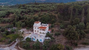 A white building with a red roof, surrounded by greenery and mountains in the background. - Amalia Country House (Zakynthos)