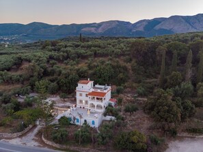 A white building with a red roof, surrounded by greenery and mountains in the background. - Amalia Country House (Zakynthos)