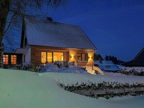 Ein Holzhaus mit geneigtem Dach, großen Fenstern und verschneiter Landschaft.