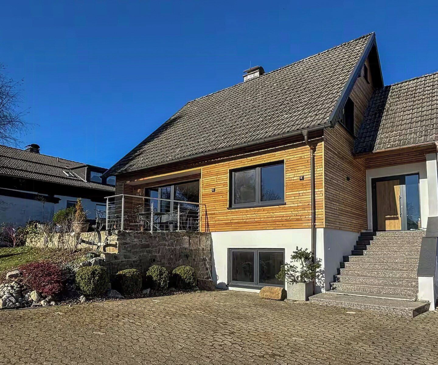 Una moderna casa a due piani con facciata in pietra, rivestimento in legno e tetto spiovente.
