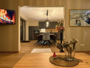 Eine moderne Küche mit dunklen Schränken, einem Essbereich mit Tisch und Stühlen, einem Fernseher und einem gerahmten Bild an der Wand.