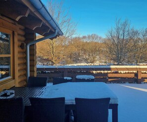 A log cabin with a snow-covered patio, outdoor seating, and a view of a snowy landscape with trees. - Round timber house in forest near Mariager (Hadsund)