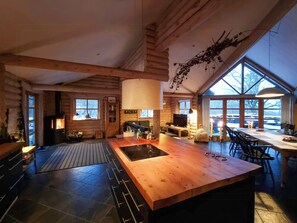 A log cabin interior with a central island, a fireplace, and large windows. - Round timber house in forest near Mariager (Hadsund)