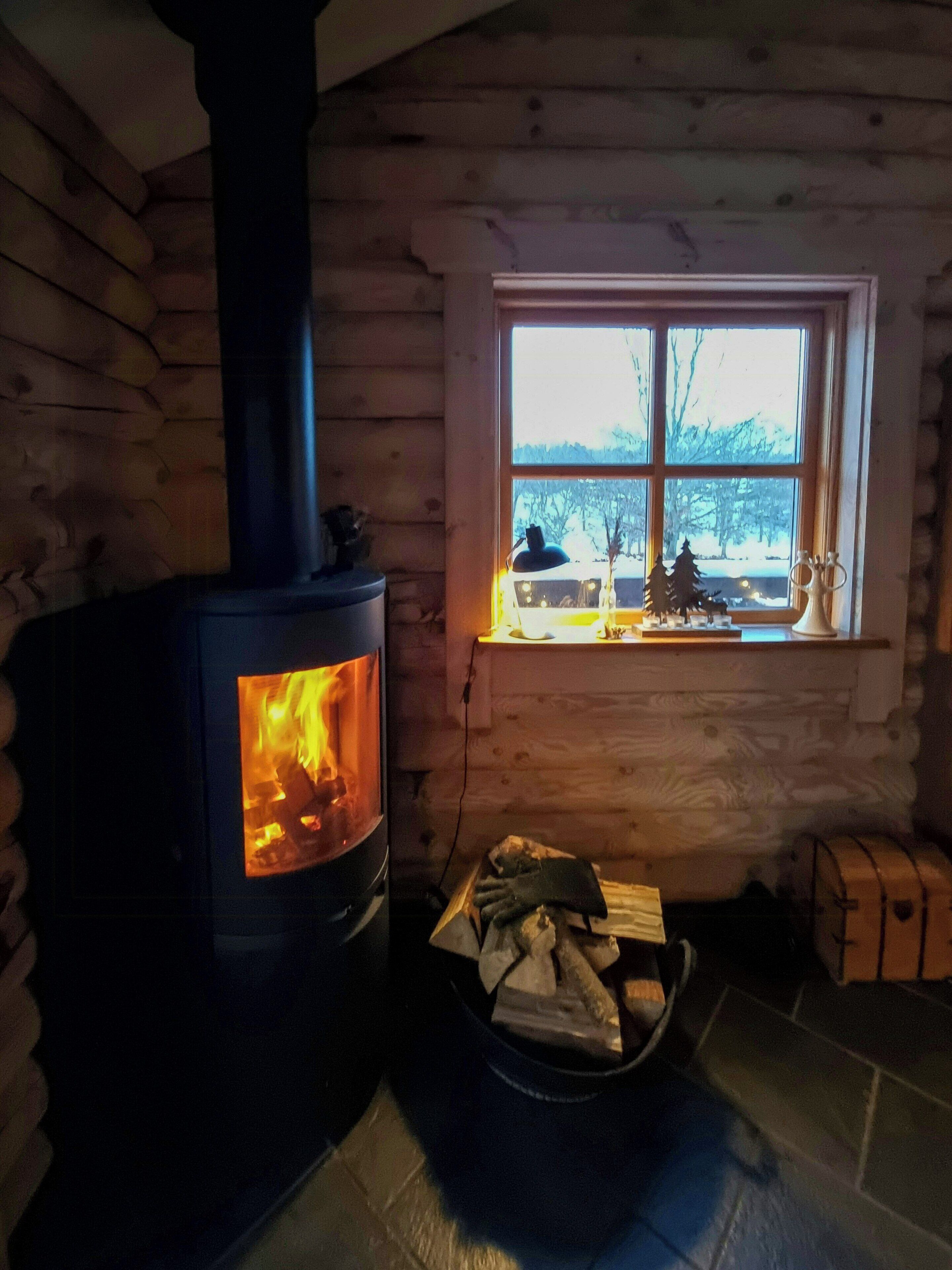 L’intérieur d’une cabane en rondins, avec un poêle à bois, une fenêtre donnant sur un beau paysage et une cheminée.