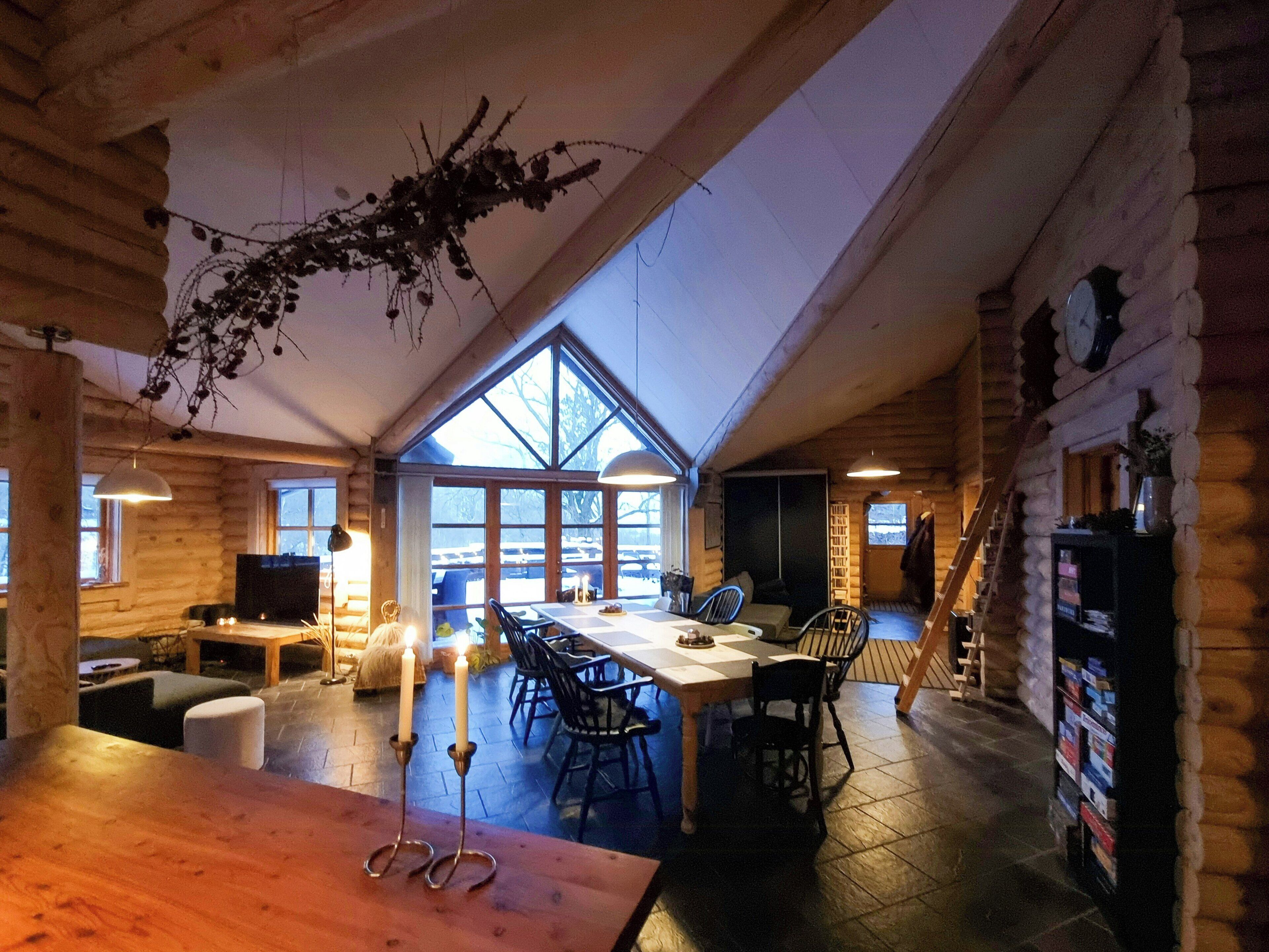 Interior de una cabaña de troncos con comedor, chimenea y un ventanal con vistas a un paisaje nevado.