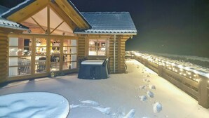 En timmerstuga med en stor glasdörr, en täckt uteplats och en snötäckt mark.