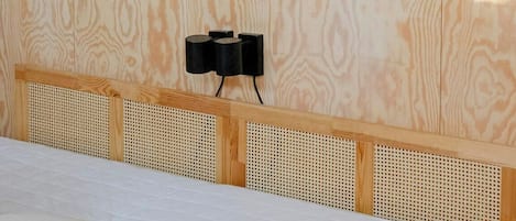 A bedroom with a bed, a headboard, a wall-mounted painting, and a wall-mounted light fixture.