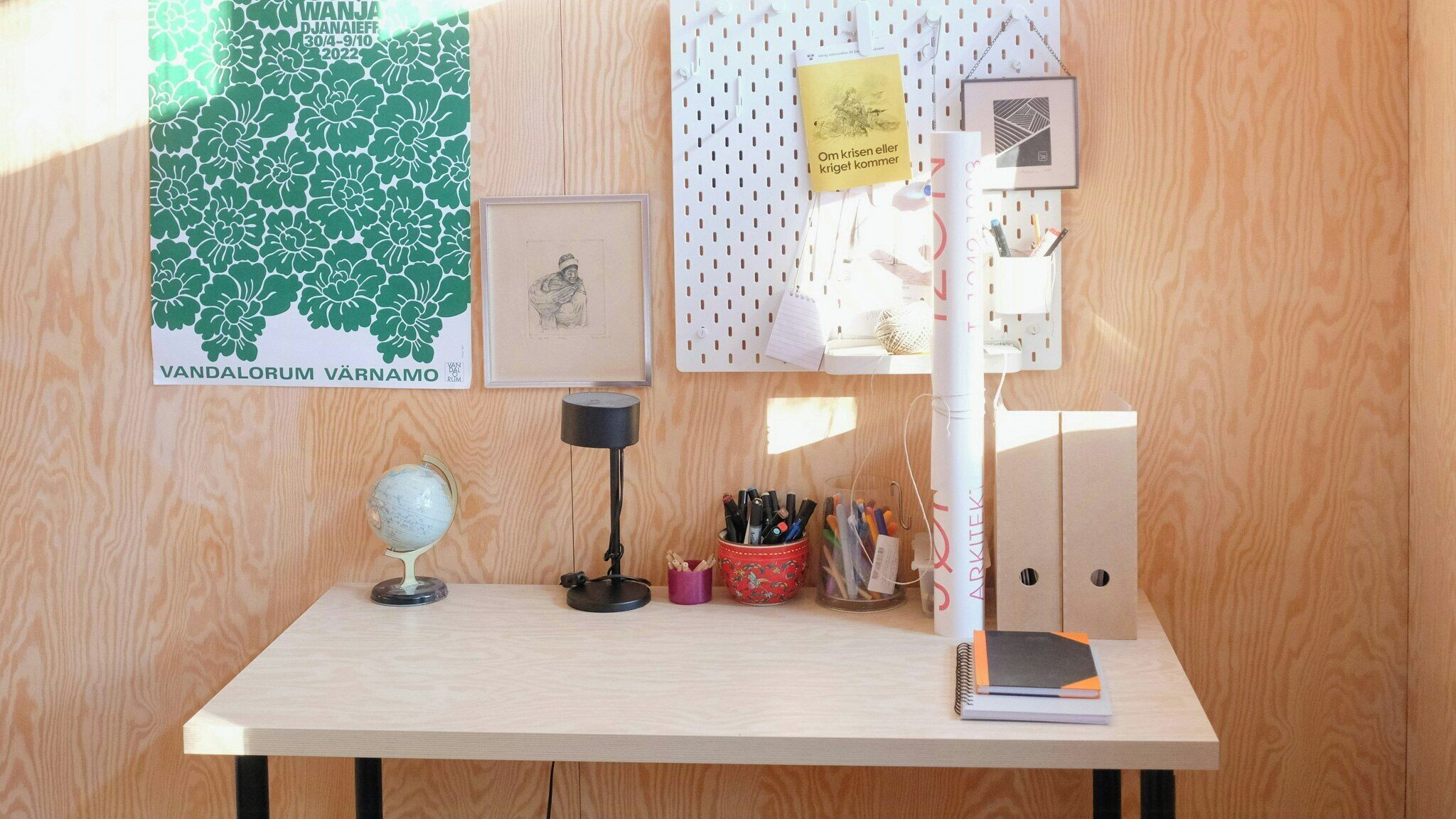 A wooden desk with a globe, a lamp, a notebook, and a corkboard with notes and pictures.