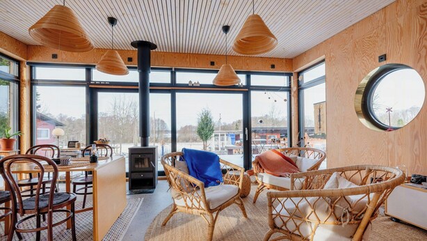 A cozy interior with wicker furniture, a fireplace, and large windows offering a view of the outdoors.