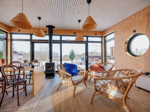 A cozy interior with wicker furniture, a fireplace, and large windows offering a view of the outdoors. - Modern functionalist cottage by Lake Vidöstern (Värnamo)