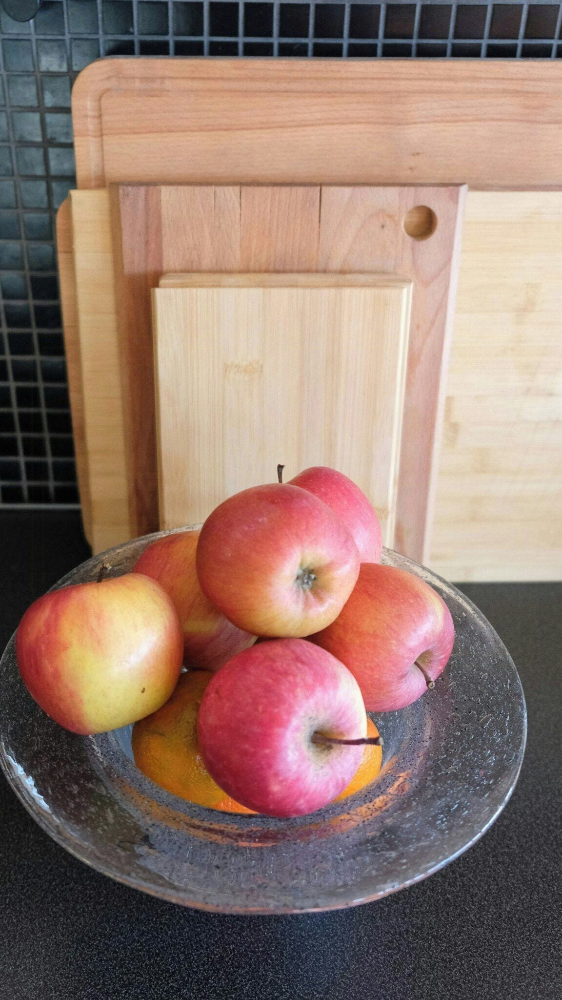 A bowl of apples on a countertop with a wooden cutting board in the background.