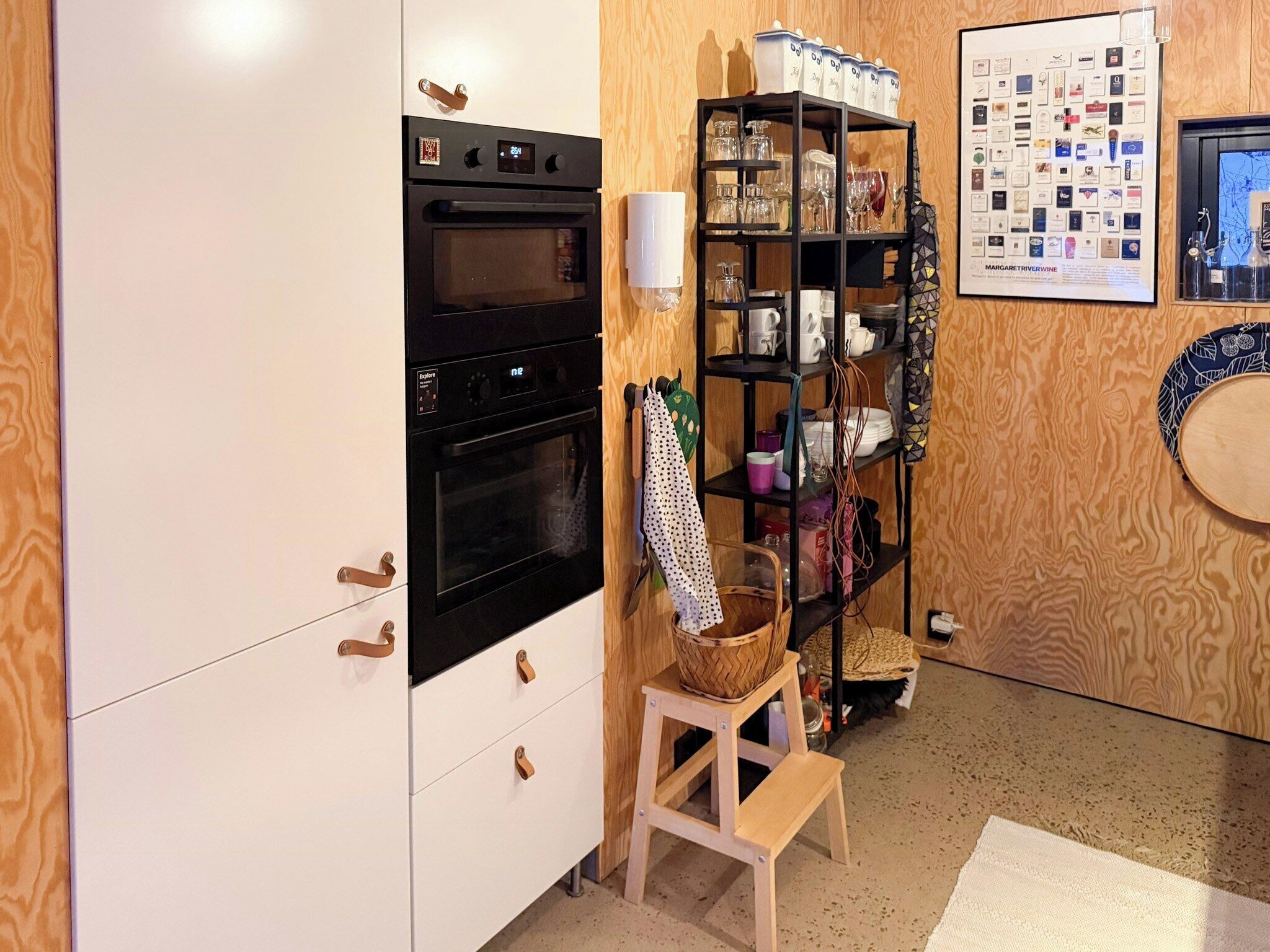 Et køkken med dobbeltovn, et træskab, en hylde med køkkenudstyr og en indramet menu på væggen.
