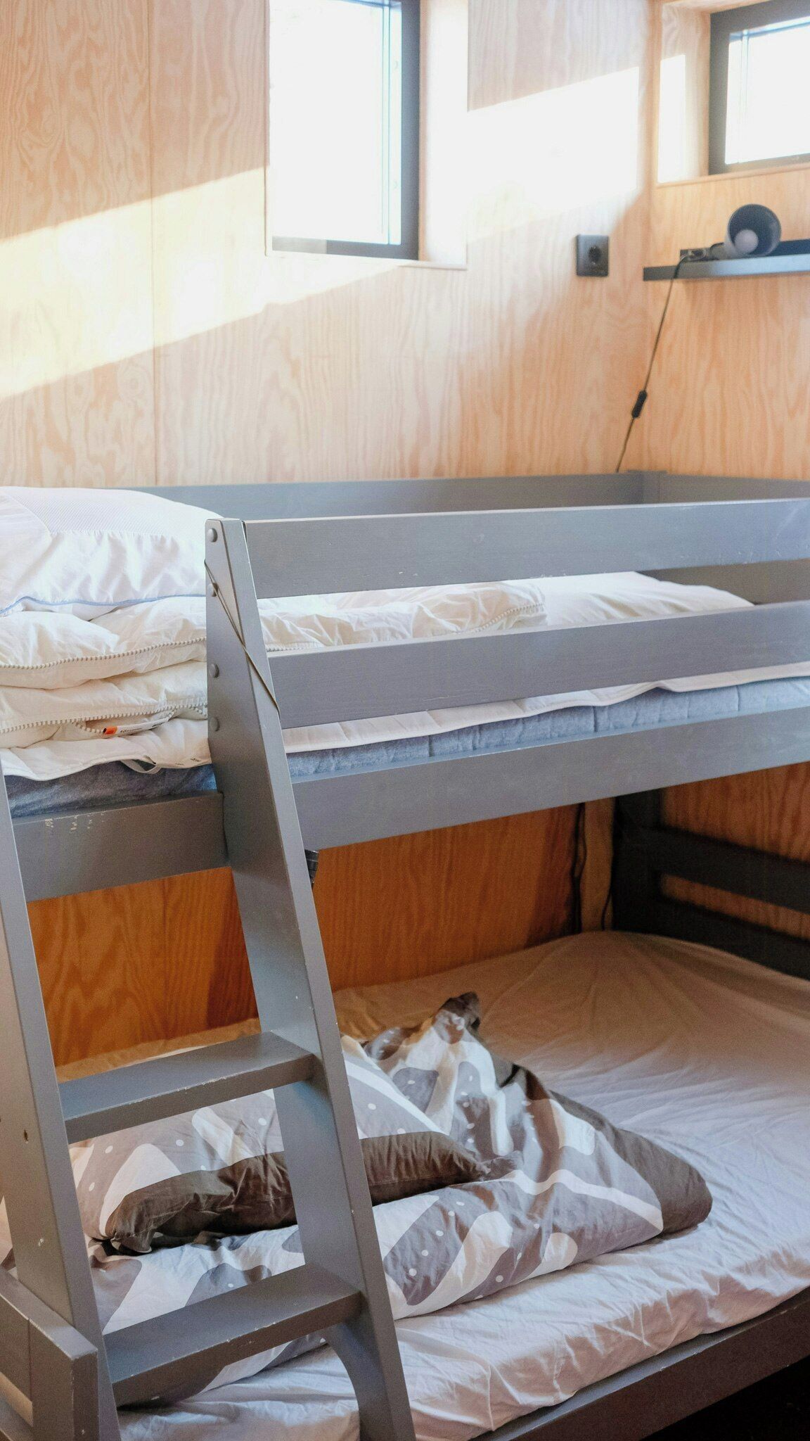 A bunk bed with a ladder, wooden walls, and a window.