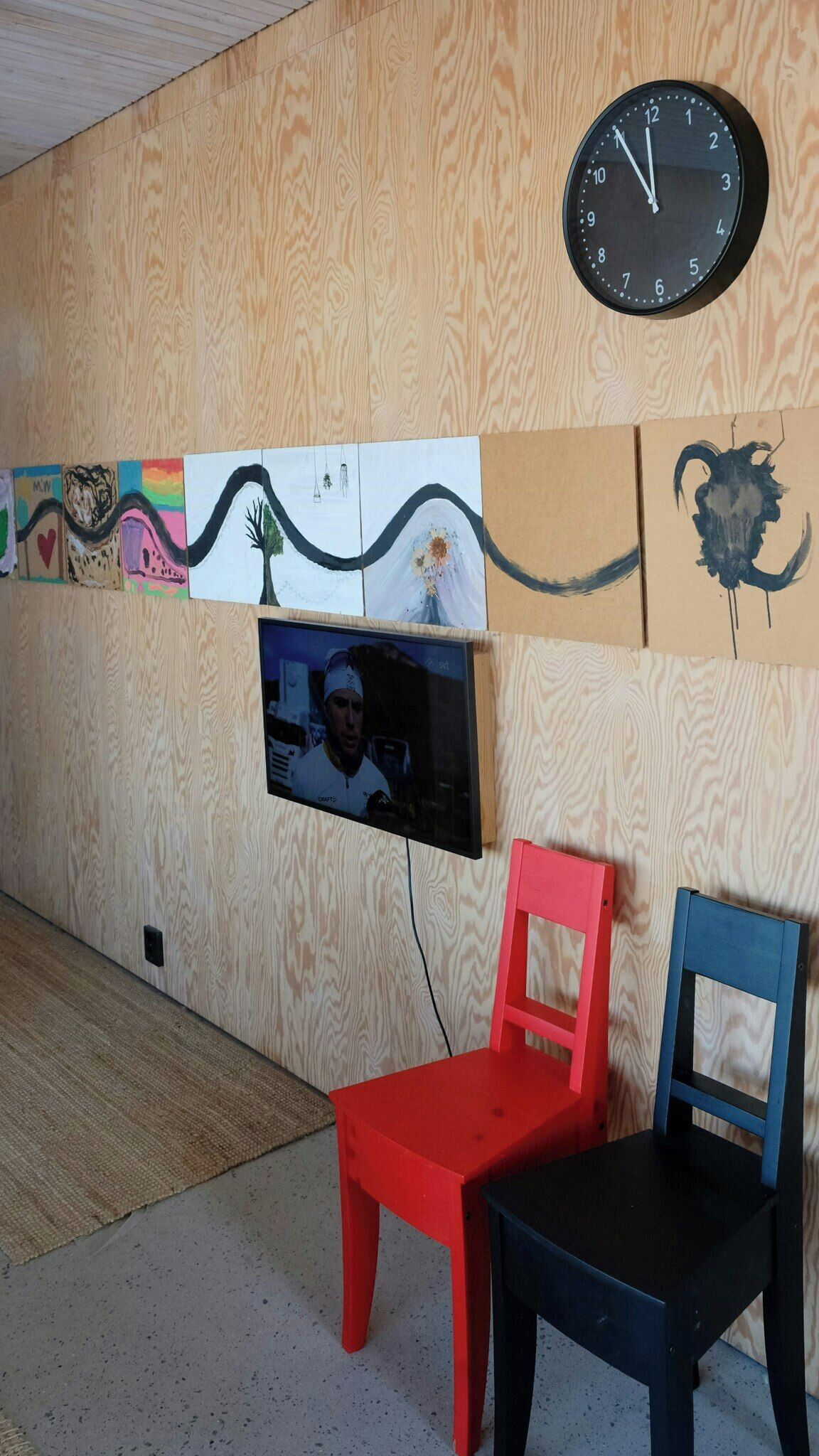 A room with a wooden wall, a clock, a television, and two chairs.