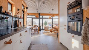 A modern kitchen with wooden ceiling, large windows, and a dining area with wicker chairs.