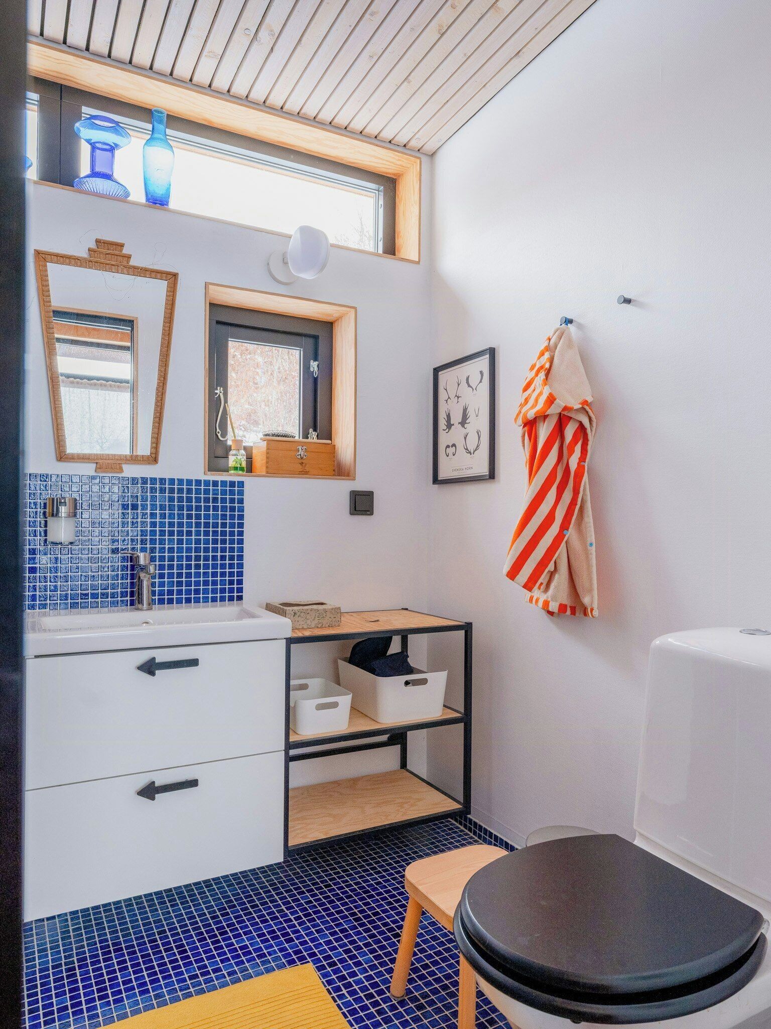 Un bagno moderno con pavimento piastrellato in blu, un mobile lavabo in legno, un water e una finestra con vista.