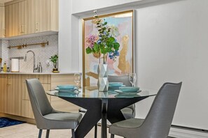Ein moderner Essbereich mit einem Glastisch, zwei grauen Stühlen und einer Blumenvase.
