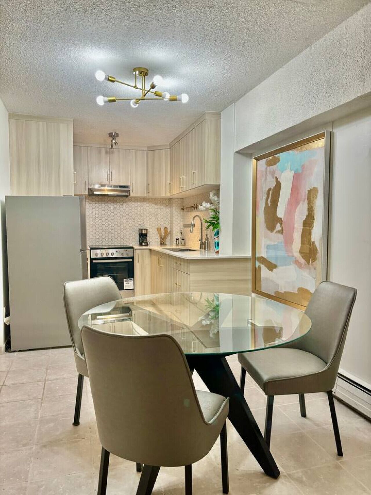 Una cocina moderna con una mesa de vidrio y sillas, un refrigerador y una cafetera.