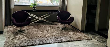 Une chambre moderne dotée d’une grande fenêtre, de deux fauteuils, d’une petite table et d’un tapis décoratif.