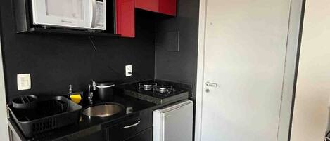 Una cocina moderna con armarios negros, un microondas blanco, un fregadero y un refrigerador pequeño.