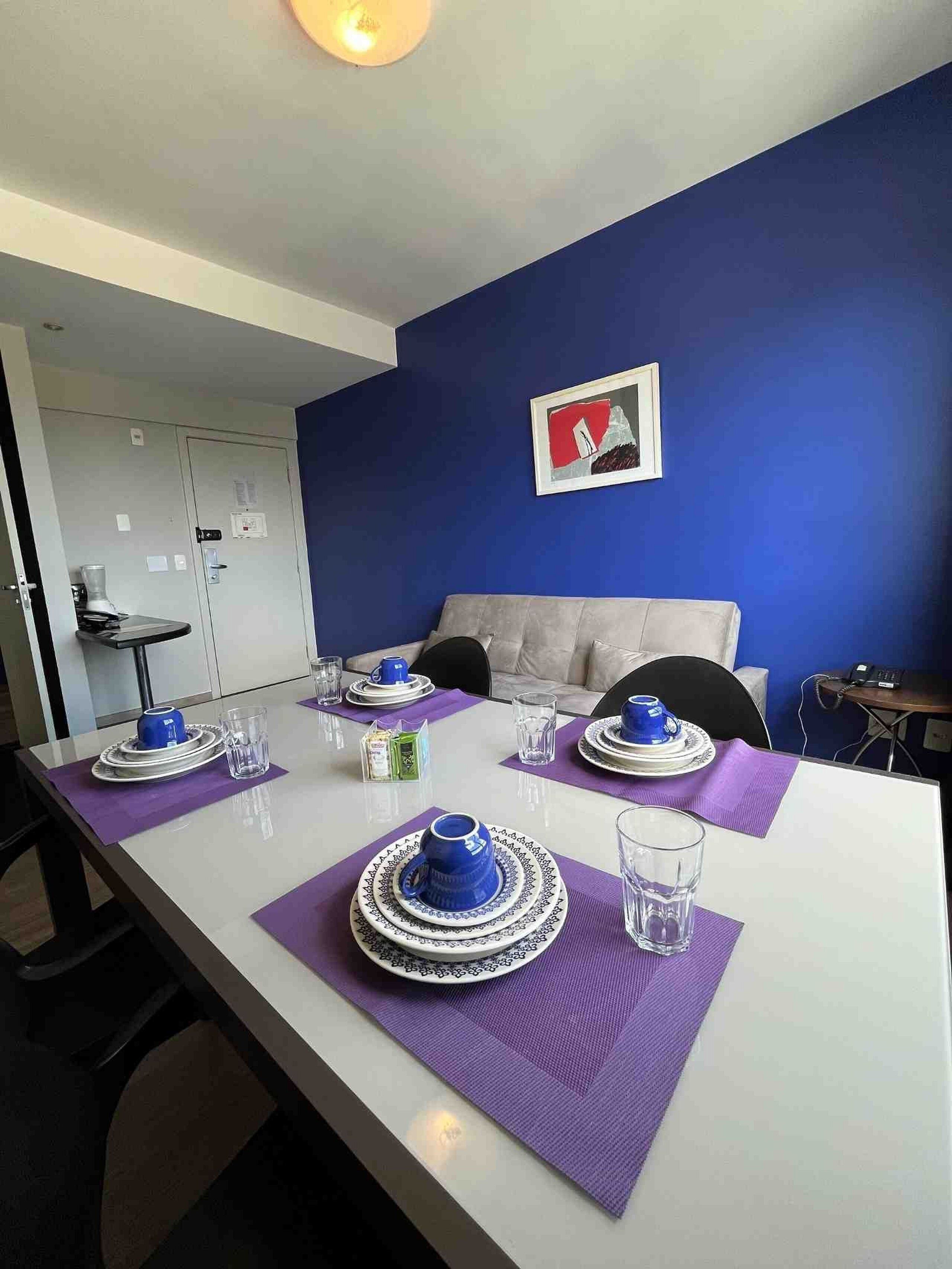 A dining area with a white table set for four, purple placemats, and blue and white tableware.