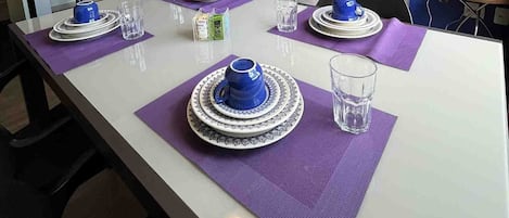 A dining area with a white table set for four, purple placemats, and blue and white tableware.