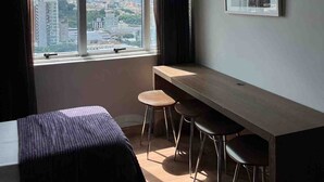 A room with a bed, a desk, two chairs, a window with a city view, and a framed picture on the wall. - LK Barro Preto 10 (Belo Horizonte)
