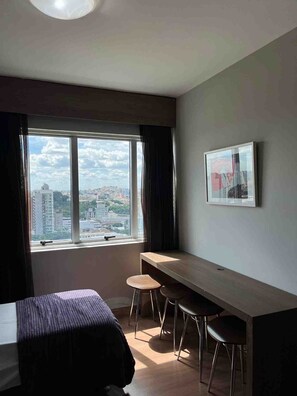 A room with a bed, a desk, two chairs, a window with a city view, and a framed picture on the wall. - LK Barro Preto 10 (Belo Horizonte)