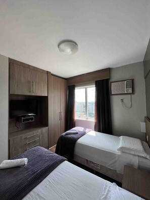 A hotel room with two beds, a television on a cabinet, a window with curtains, and a city view. - LK Barro Preto 10 (Belo Horizonte)