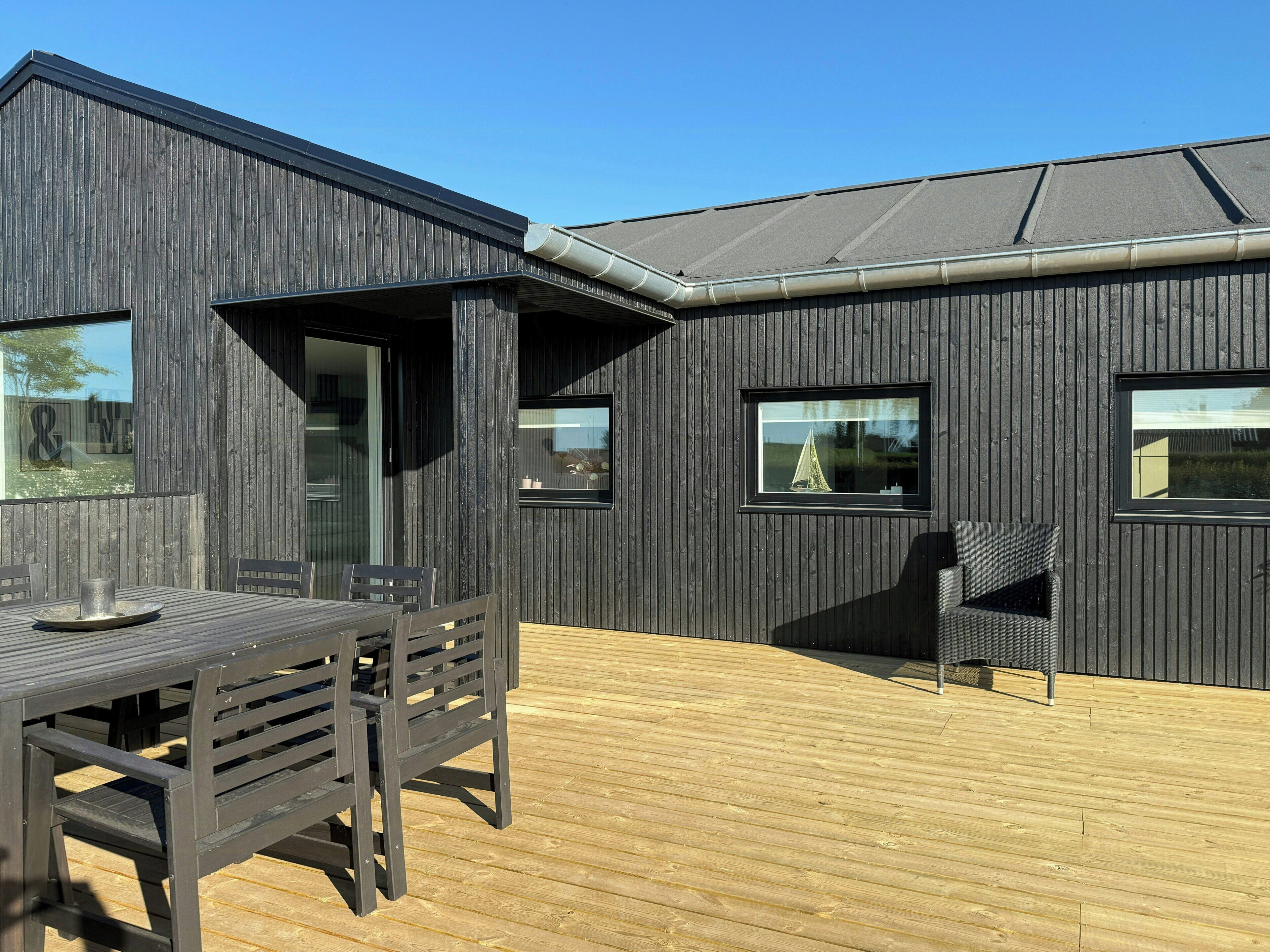 Ein modernes Gebäude mit dunkler Fassade, einer Holzterrasse und einem Tisch mit Stühlen.