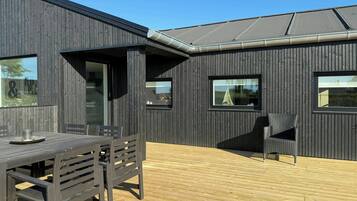 Ein modernes Gebäude mit dunkler Fassade, einer Holzterrasse und einem Tisch mit Stühlen.