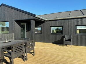 Un bâtiment moderne à l’extérieur sombre, doté d’une terrasse en bois et d’une table avec des chaises.