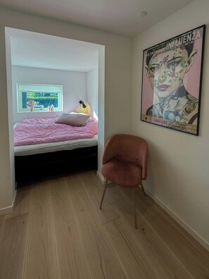 Une chambre à coucher avec un lit, une chaise, une affiche et une fenêtre.
