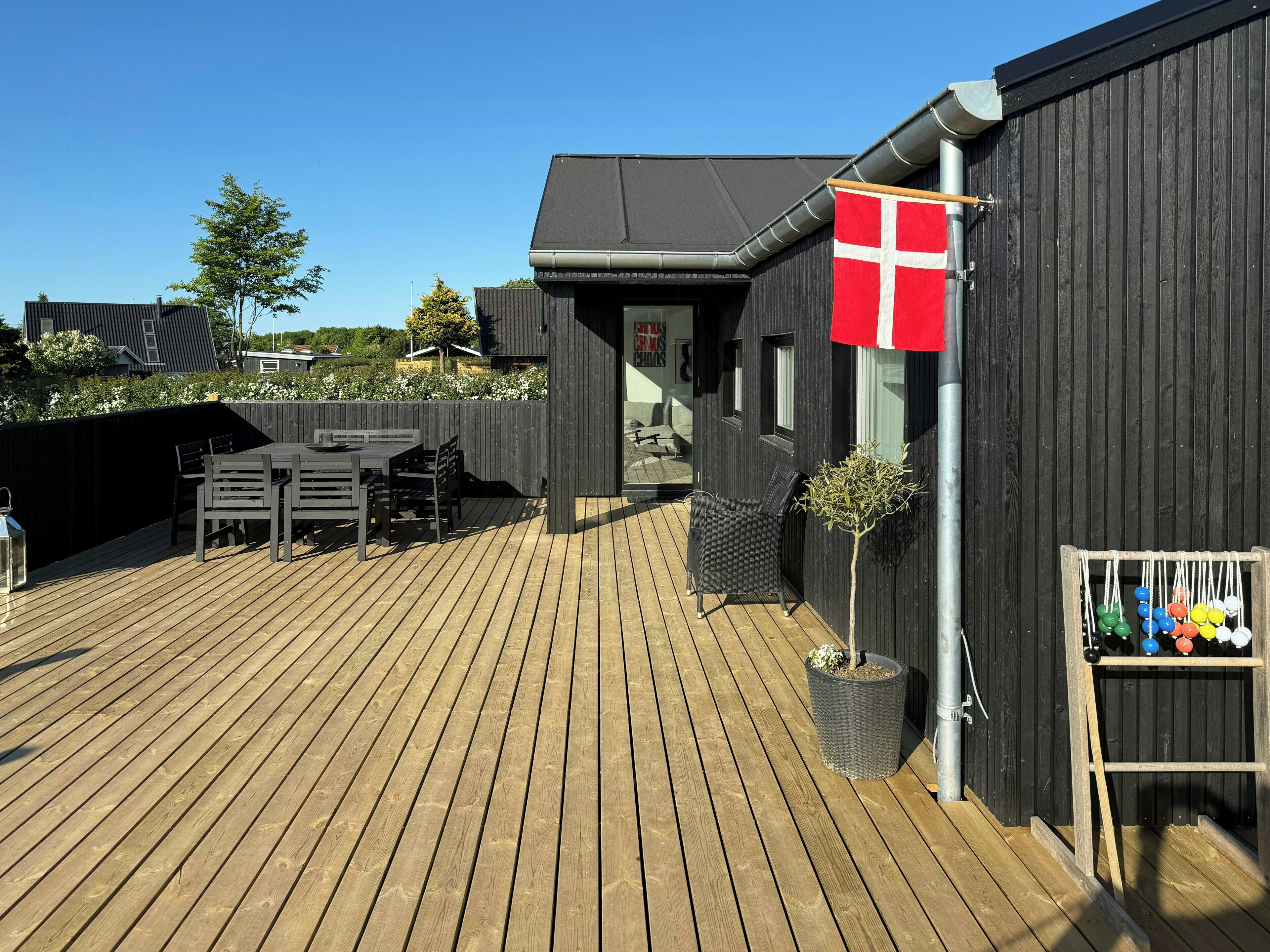 Eine Holzterrasse mit Sitzgelegenheiten im Freien, einer Flagge und einer kleinen Pflanze.