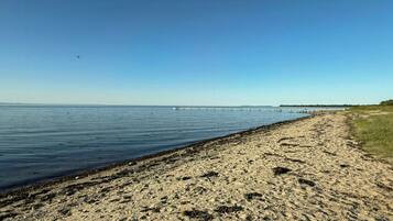 Ein sandiger Strand mit ruhigem Wasser, blauem Himmel und weiter Küste.