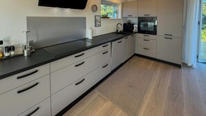 Une cuisine moderne avec un plan de travail noir, des appareils en acier inoxydable et un revêtement de sol en bois clair.